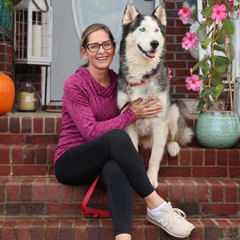 woman in purple shirt sitting on the porch with her husky