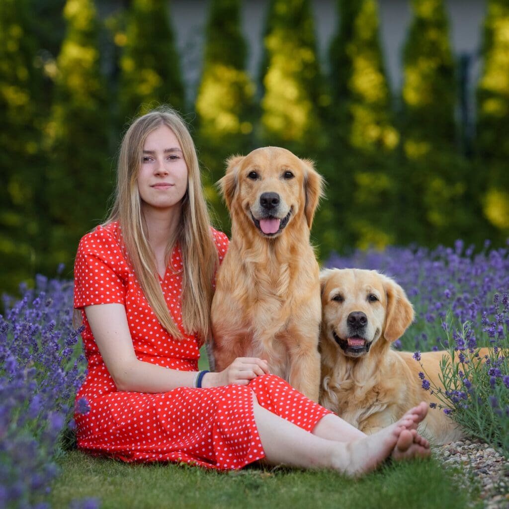 Blonde woman with two golden retrievers sitting in the garden next to lavender